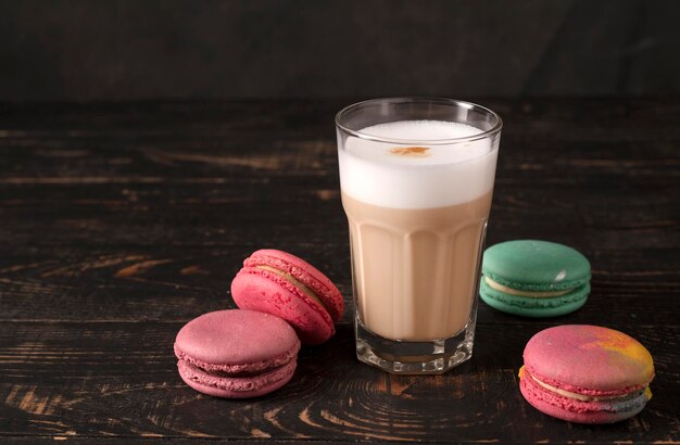 caffè con latte in un bicchiere con macarons. latte su fondo di legno scuro. Bevanda alla moda. Umore oscuro