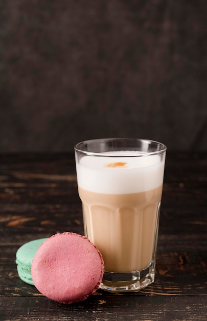 caffè con latte in un bicchiere con macarons. latte su fondo di legno scuro. Bevanda alla moda. Umore oscuro