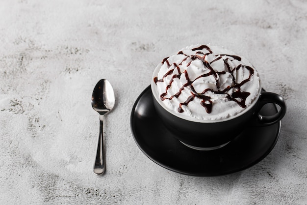 Caffè con panna montata e topping al cioccolato. Caffè ghiacciato in tazza scura isolato su sfondo di marmo luminoso. Vista dall'alto, copia spazio. Pubblicità per menu bar. Menu della caffetteria. Foto orizzontale.