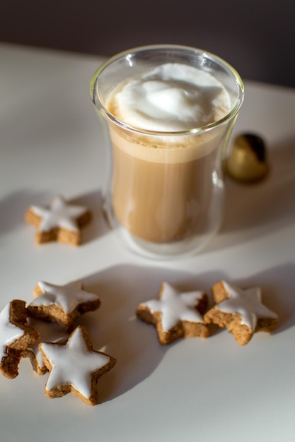 Caffè con schiuma di latte bianca su un tavolo bianco tra biscotti stellati