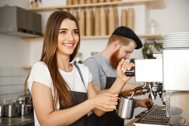 Caffè concetto di business - ritratto di signora barista in grembiule preparazione e vapore latte per l&#39;ordine di caffè con il suo partner mentre in piedi al caffè.