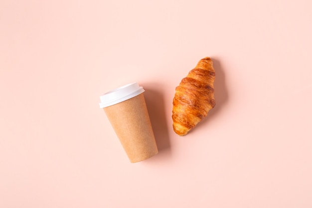 Caffè da asporto in una tazza di carta con croissant, vista dall'alto.