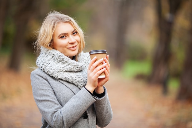 Caffè da portar via. Giovane donna con caffè nel parco di autunno