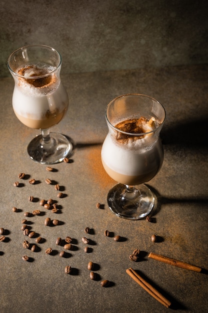 Caffè dalgona fatto in casa su sfondo scuro. Accanto a chicchi di caffè e bastoncini di cannella.