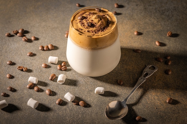 Caffè dalgona fatto in casa su sfondo scuro. Accanto a chicchi di caffè e marshmallow.