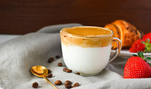 Caffè Dalgona In una tazza trasparente, fragole, croissant su una superficie scura. Bevanda di tendenza. Caffè del mattino. Colazione salutare.