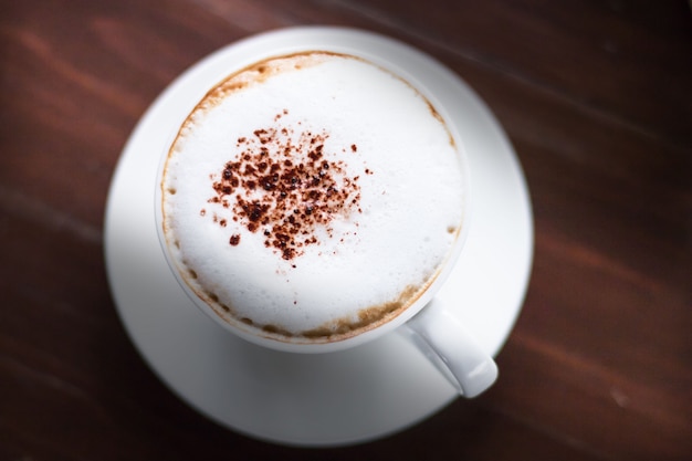 Caffè del cappuccino con la guarnizione del cacao in tazza bianca sopra fondo di legno scuro