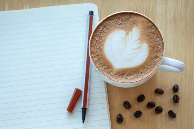 Caffè di arte del latte e chicchi di caffè arrostiti con papernote a tempo di mattina con luce solare sopra