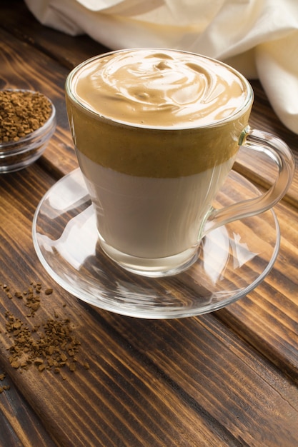 Caffè di Dalgona nella tazza di vetro nella superficie di legno marrone. Posizione verticale.