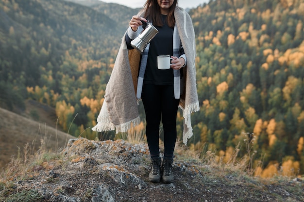 Caffè di versamento della giovane donna nelle montagne