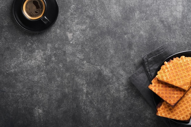 Caffè e cialde olandesi Caffè espresso e cialde olandesi o biscotti con cialde sciroppo con cioccolato su vecchio tavolo di cemento nero Biscotti perfetti con cialde sciroppo per colazione Vista dall'alto Mock up