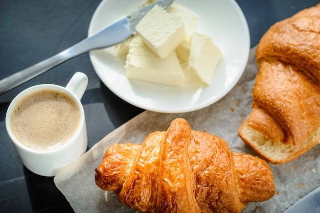 Caffè e croissant con burro su sfondo nero