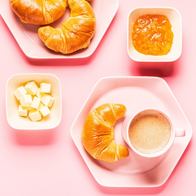 Caffè e croissant per colazione su uno sfondo rosa, vista dall'alto,