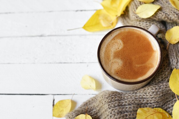 Caffè e foglie di autunno caldi su fondo di legno bianco