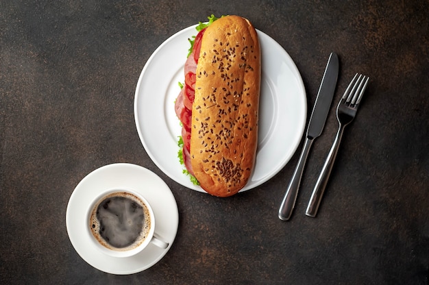 caffè e un panino con salsiccia, formaggio e insalata su uno sfondo di pietra. con spazio copia per il tuo testo