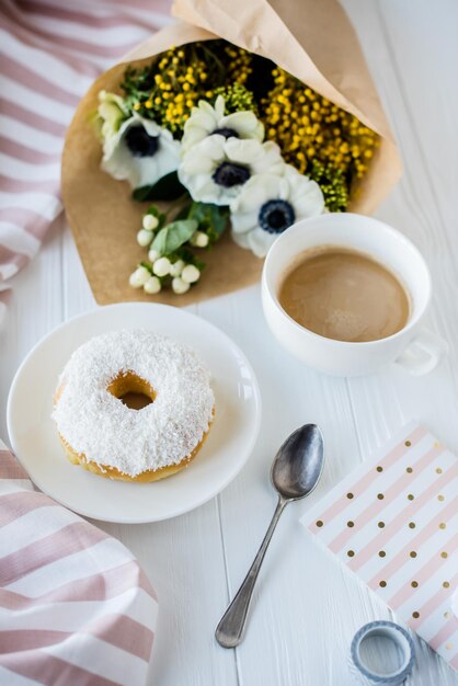 Caffè e una ciambella con fiori freschi