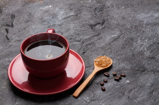 Caffè e zucchero rossi della tazza in cucchiaio su roccia