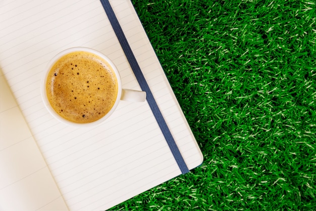 Caffè espresso aperto della tazza di caffè del blocchetto per appunti in bianco su un'erba verde