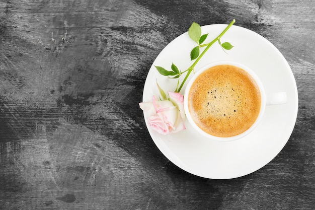 Caffè espresso in una tazza bianca e una rosa rosa su uno sfondo scuro. Vista dall'alto, copia spazio. Sfondo di cibo