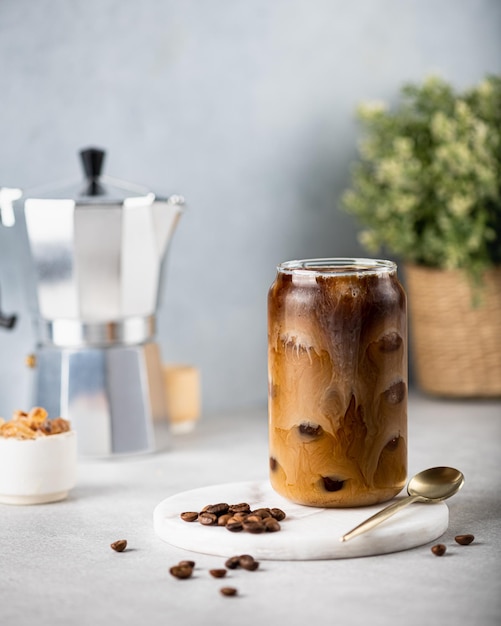 Caffè freddo con cubetti di ghiaccio in un bicchiere su uno sfondo chiaro i chicchi di caffè sono sparsi nelle vicinanze