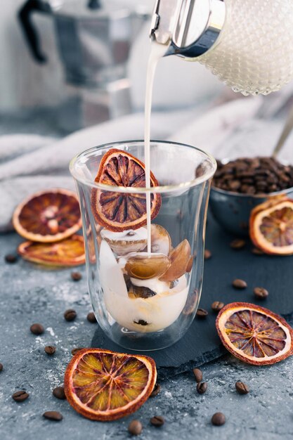 Caffè freddo con latte Bevanda estiva Versare il latte nel caffè con cubetto di ghiaccio su sfondo grigio