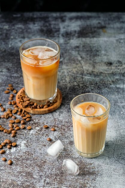 Caffè freddo in un bicchiere alto con panna versata, cubetti di ghiaccio e grani su un vecchio tavolo di legno rustico