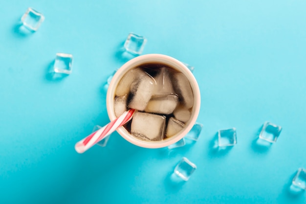 Caffè ghiacciato rinfrescante in un bicchiere e cubetti di ghiaccio su una superficie blu. Concetto estate, cola con ghiaccio, cocktail rinfrescante, sete. Vista piana, vista dall'alto