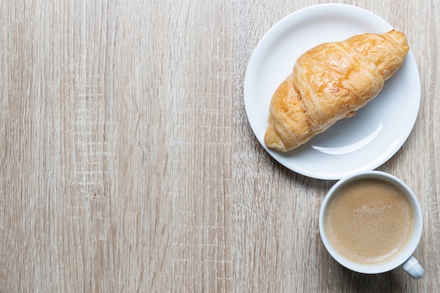 Caffè in tazza bianca e croissant sulla tavola di legno, concetto della prima colazione