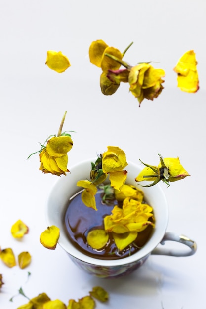 Caffè in tazza con rose gialle in levitazione su bianco