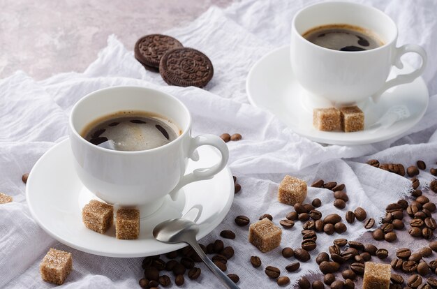 Caffè in tazza e piattino su sfondo chiaro con chicchi di caffè e zucchero di canna.