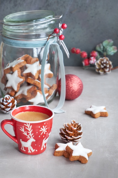 Caffè in tazza rossa di Natale e gustosi biscotti di zenzero stella in un barattolo di vetro con decorazioni invernali