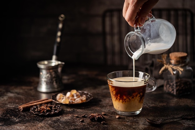 Caffè in un bicchiere con panna versata su zucchero e chicchi di caffè su sfondo scuro