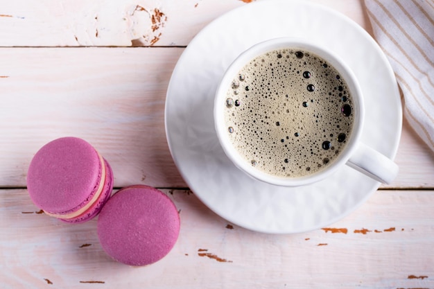 Caffè in una tazza bianca e due amaretti rosa su uno sfondo di legno chiaro vista dall'alto