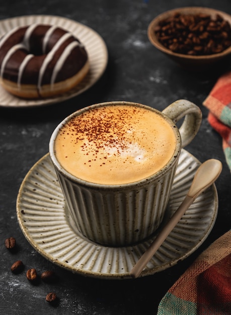 Caffè in una tazza con una ciambella e chicchi di caffè, scuro