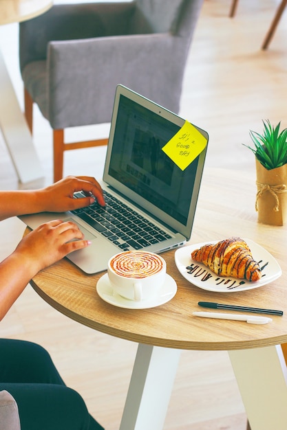 Caffè, laptop e cornetti per mostrare una colazione di lavoro sul tavolo dell'ufficio in mattinata.