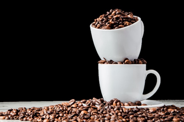 Caffè nero in tazza bianca e chicchi di caffè su fondo nero.