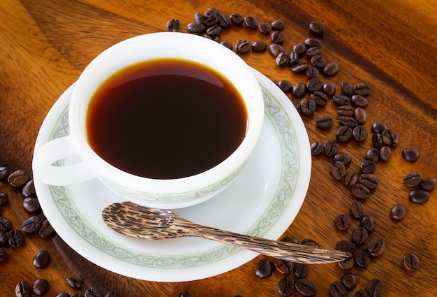 Caffè nero in tazza di caffè bianco sul fondo di legno d'annata della tavola
