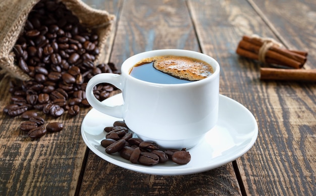 Caffè nero in una tazza bianca, chicchi di caffè, bastoncini di cannella su un vecchio fondo di legno.