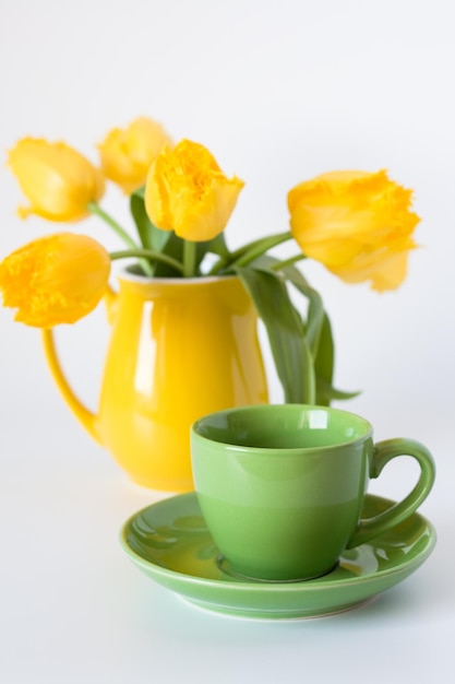 Caffè nero in una tazza verde e un mazzo di tulipani gialli in un vaso giallo