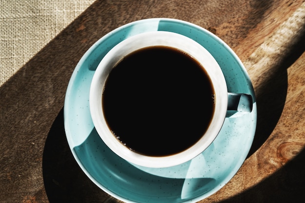 Caffè nero piatto in una tazza sul fondo del tagliere, ombre del sole mattutino.