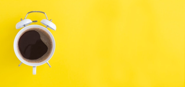 Caffè nero sul quadrante della sveglia bianca sullo sfondo giallo Copia spazio Vista dall'alto