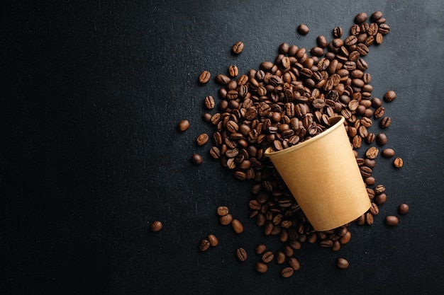 Caffè o concetto di scarto zero. Chicchi di caffè in bicchiere di carta su sfondo scuro.