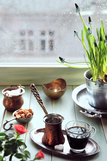 Caffè orientale nella tradizionale caffettiera turca in rame con fiori sul davanzale della finestra. Davanzale in legno con vaso di fiori di giacinto. Giornata di pioggia fredda in primavera. Scena accogliente, concetto hygge.