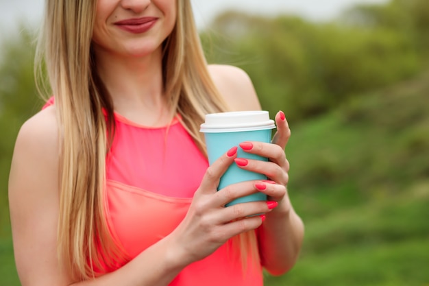 Caffè per andare tazza turchese nelle mani della donna con manicure rosa.