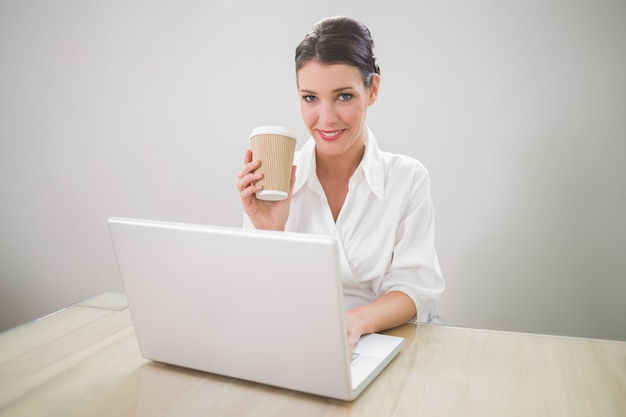 Caffè splendido della tenuta della donna di affari mentre per mezzo del computer portatile