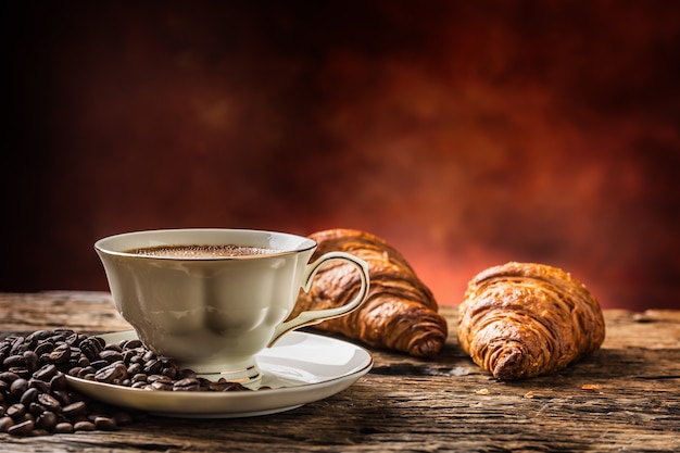 Caffè. Tazza di caffè croissant e chicchi di caffè. Tazza vintage e vecchio tavolo in rovere.