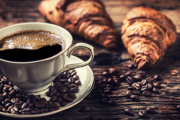 Caffè. Tazza di caffè croissant e chicchi di caffè. Tazza vintage e vecchio tavolo in rovere.