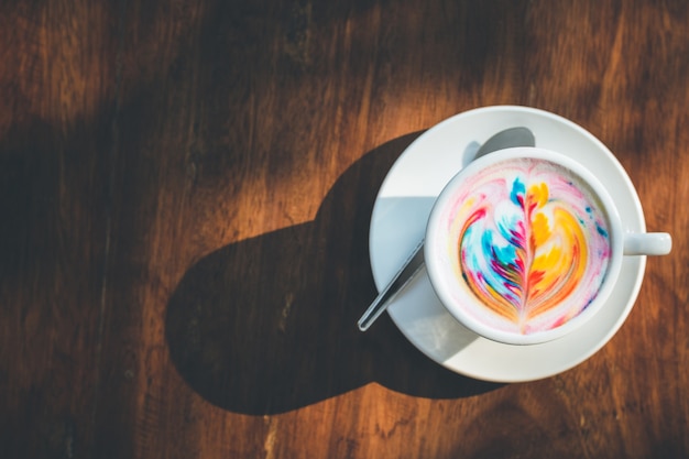 Caffè variopinto del latte dell&#39;arcobaleno in tazza bianca sulla tavola di legno con lo spazio della copia per testo o progettazione