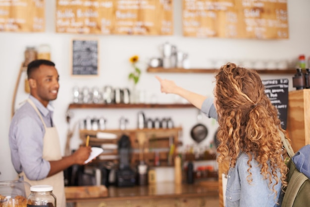 Caffetteria donna e indicando il menu sul muro con note e servizio del barista per una buona esperienza del cliente Cameriere maschio che scrive signora e parla con decisione di scelta e ordine dal panificio