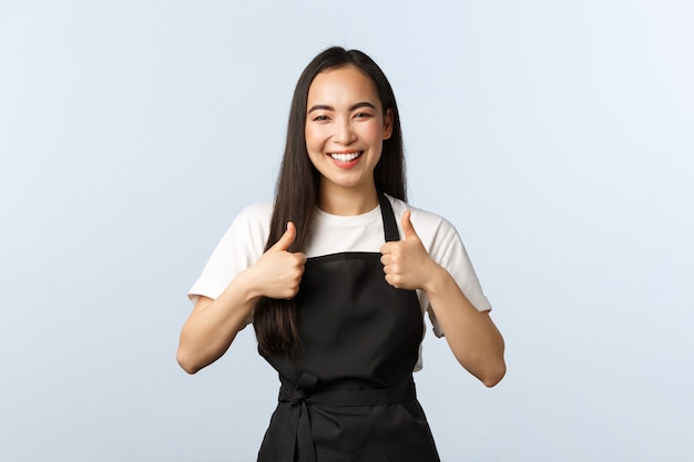 Caffetteria, piccola impresa e concetto di avvio. Personale femminile asiatico sorridente allegro del caffè, barista sul lavoro che mostra pollice in su, grembiule d'uso. L'impiegato della ragazza carina consiglia di visitare un bel posto, buon cibo?